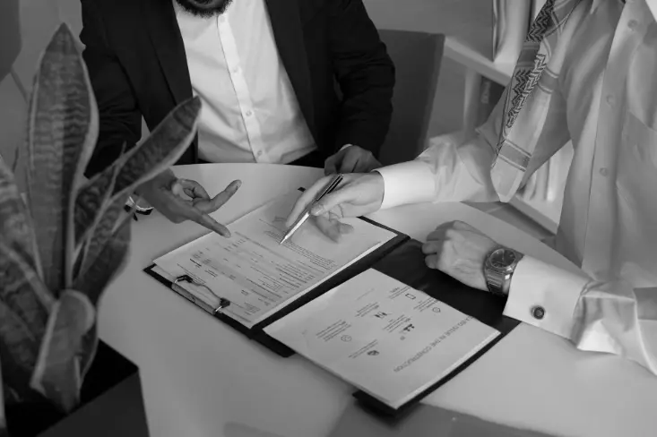 two men sitting at a table with papers and a pen